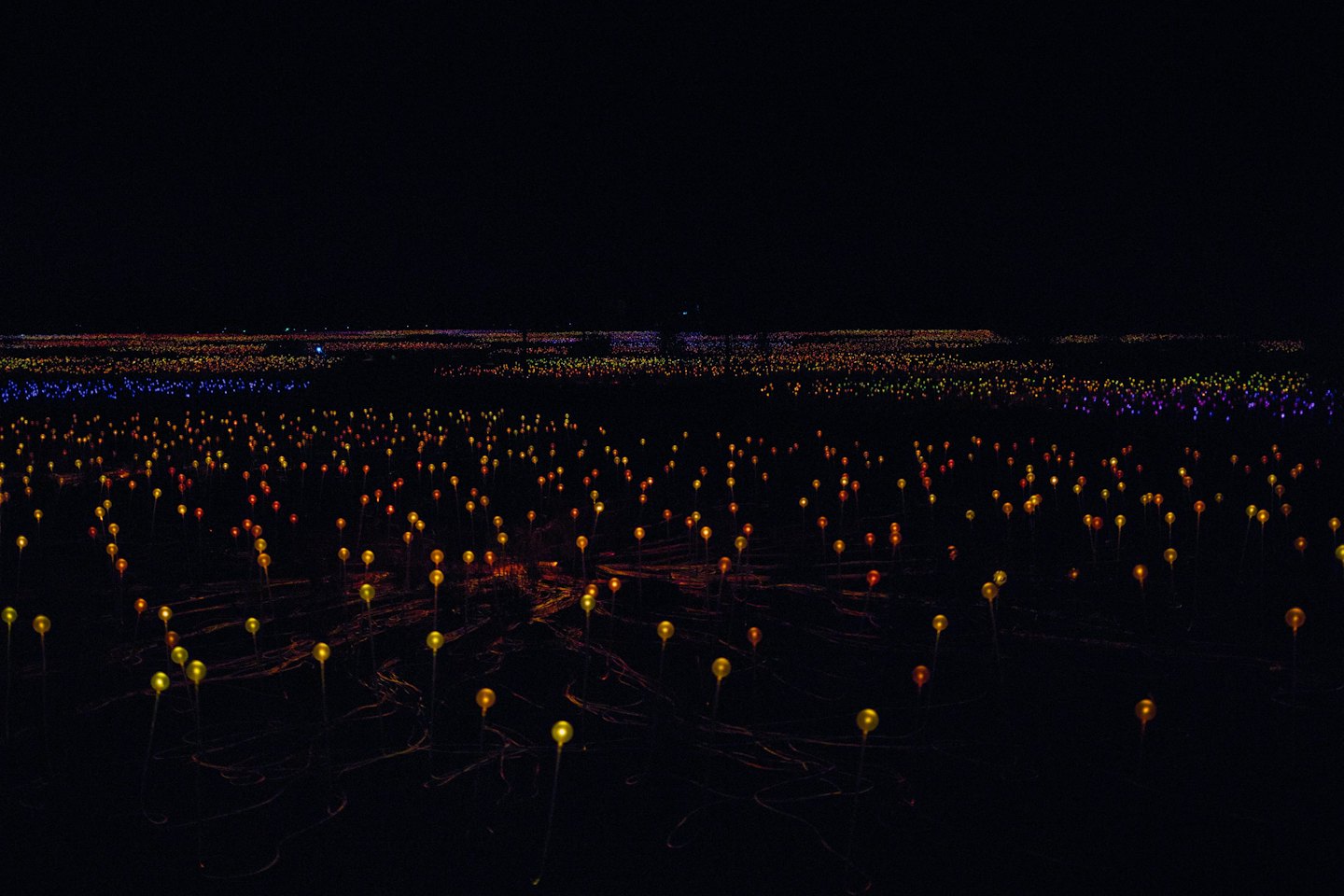Colorful glowing artificial lights illuminate a dark open field.