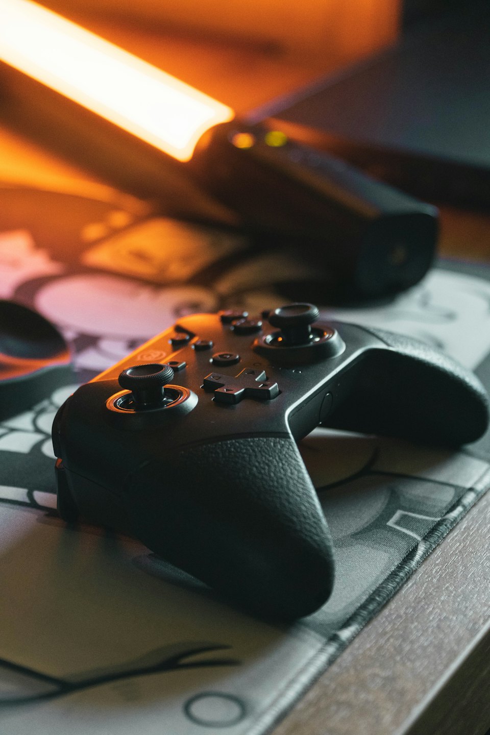 Black gaming controller on a patterned mat on a desk.